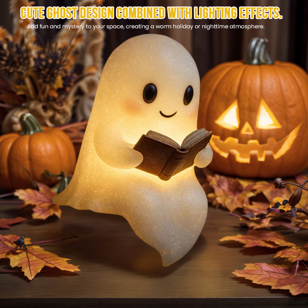 Cute LED ghost night light holding an open book, glowing on a wooden table with pumpkins